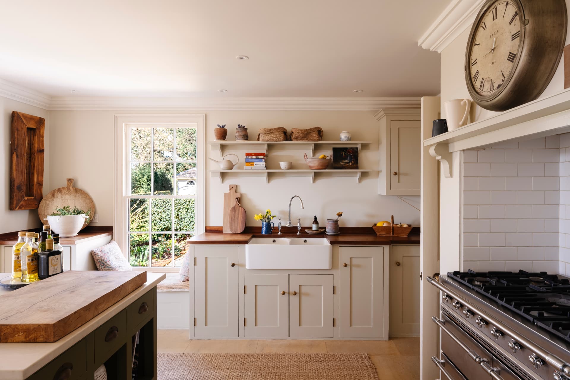 A pale shaker kitchen with timber worktops, a butler sink beneath a sash window, open shelving and a range set into a painted chimney breast
