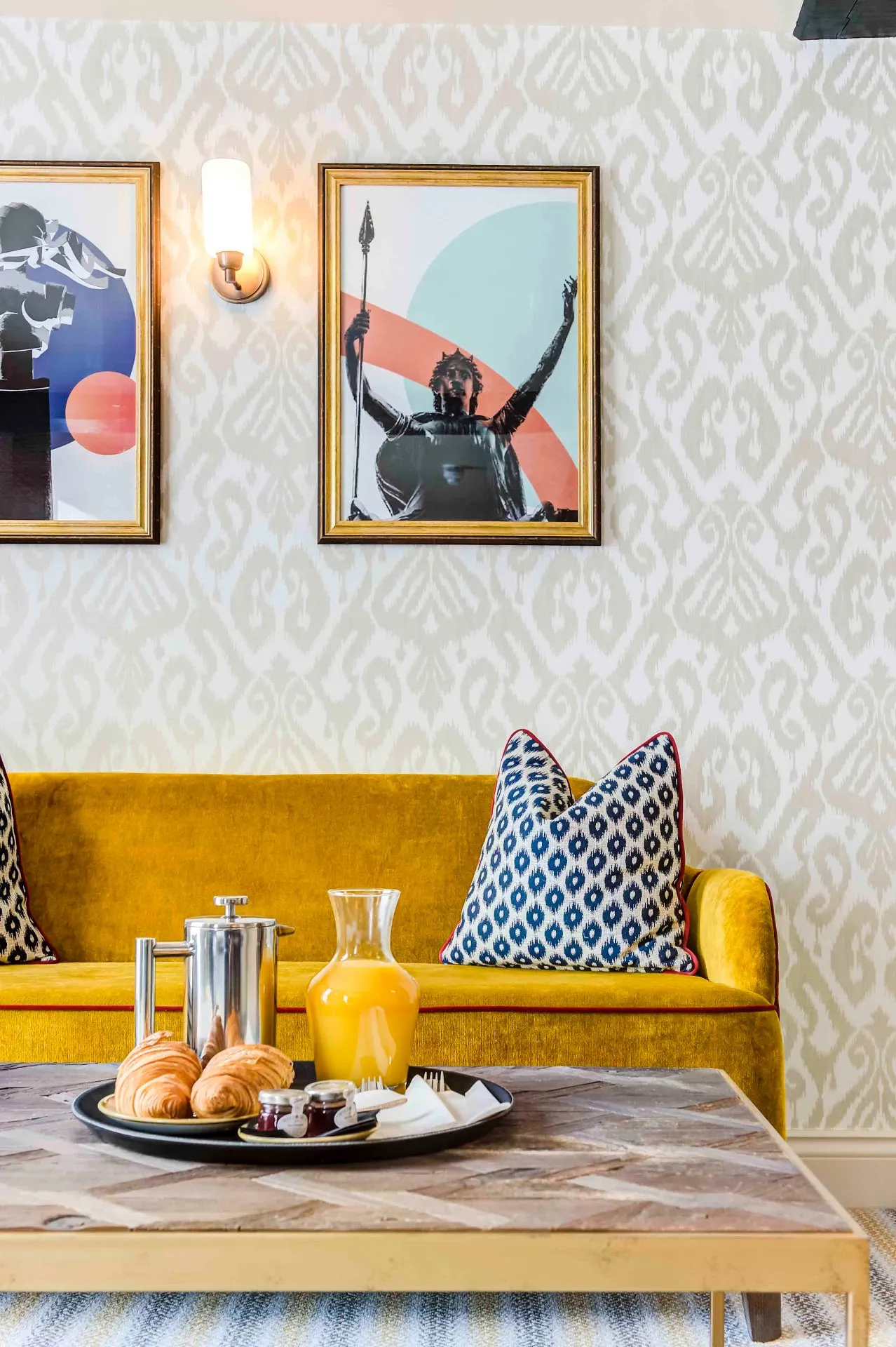 A hotel lounge with a mustard velvet banquette, bold patterned wallpaper and gallery-hung artwork