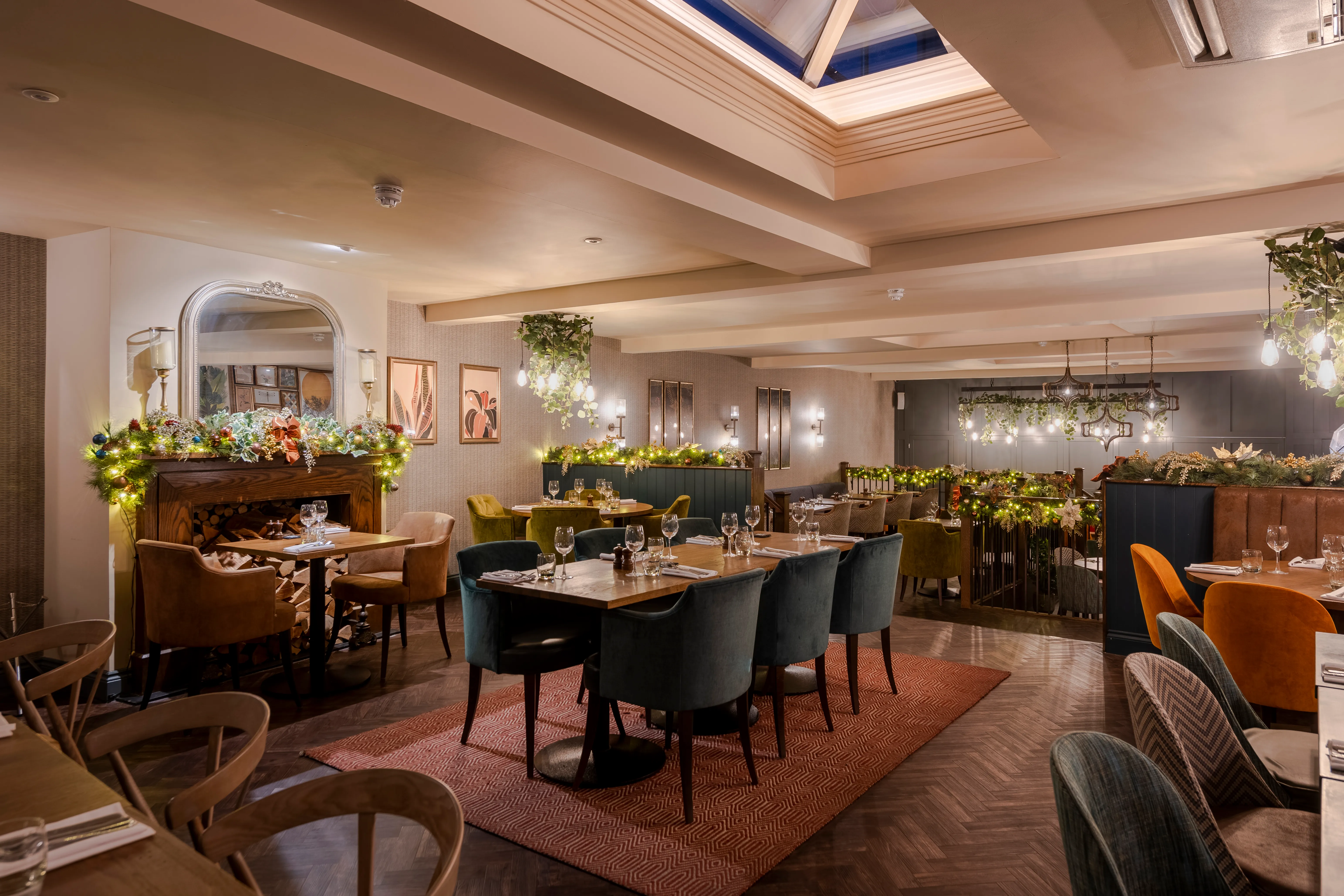 A restaurant dining room with mixed banquette and chair seating, planting dividers and warm ambient lighting