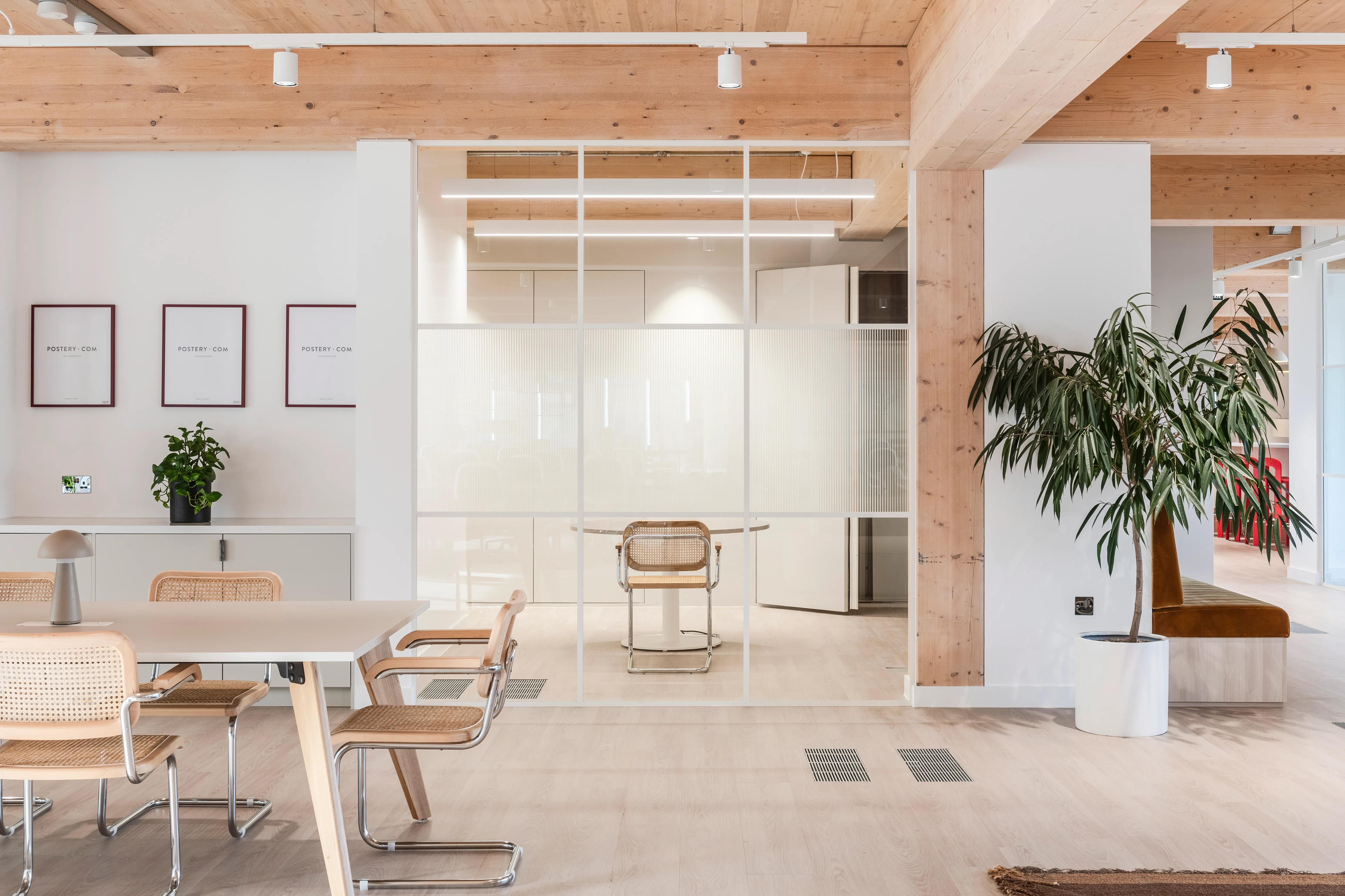 An open-plan office beneath exposed timber beams, with floor-to-ceiling glazing onto the city, sliding glass partitions and potted plants dividing the space