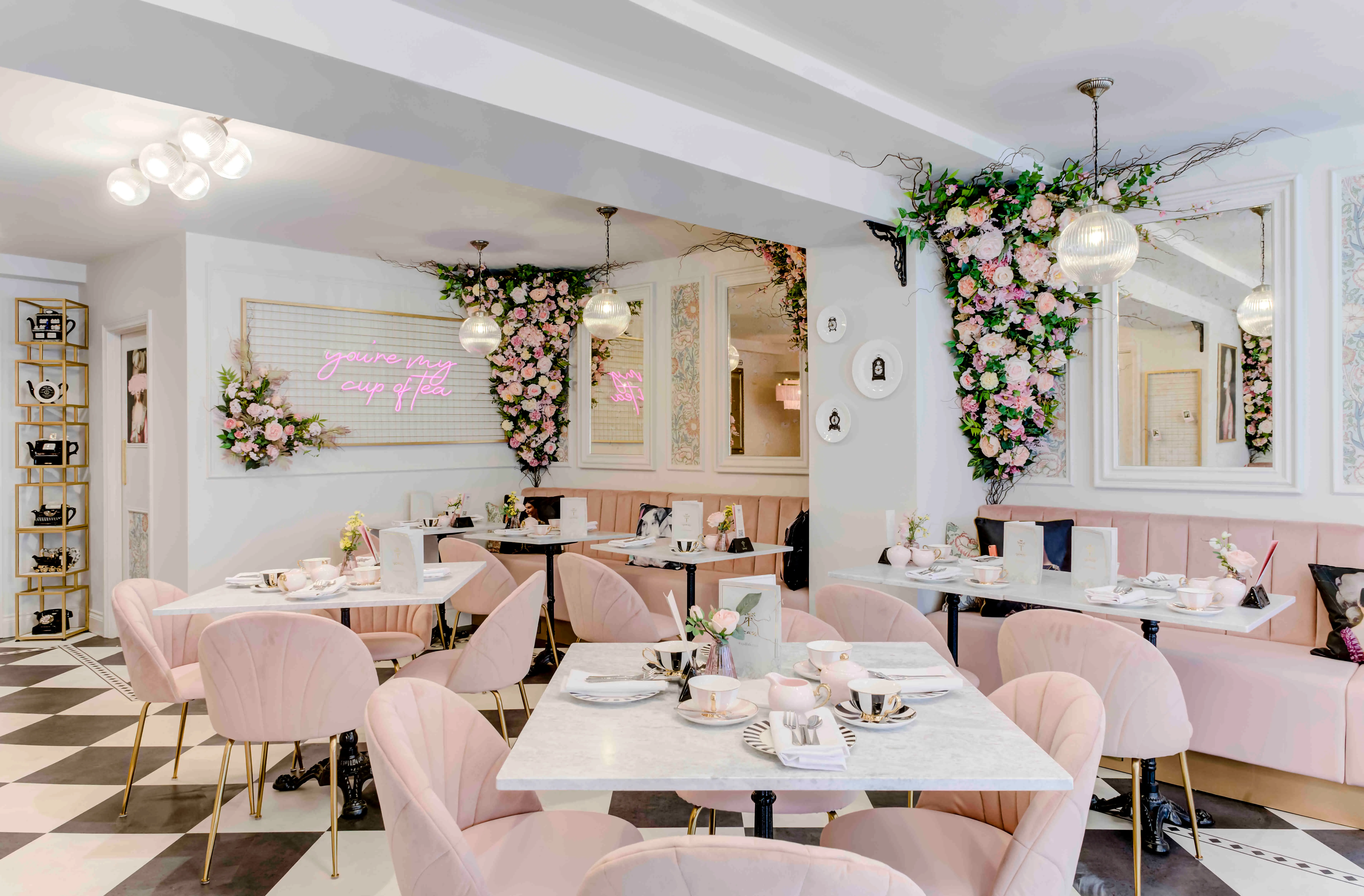 A pink and marble-topped tearoom with blush upholstered chairs and a black-and-white chequerboard floor, laid for afternoon tea
